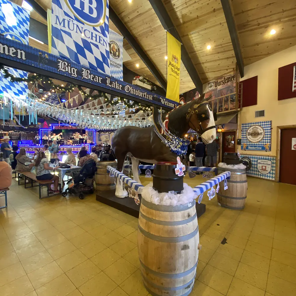 Big Bear Lake Oktoberfest beer hall with Bavarian flags, wooden horse statue, and families enjoying food, beer, and live music