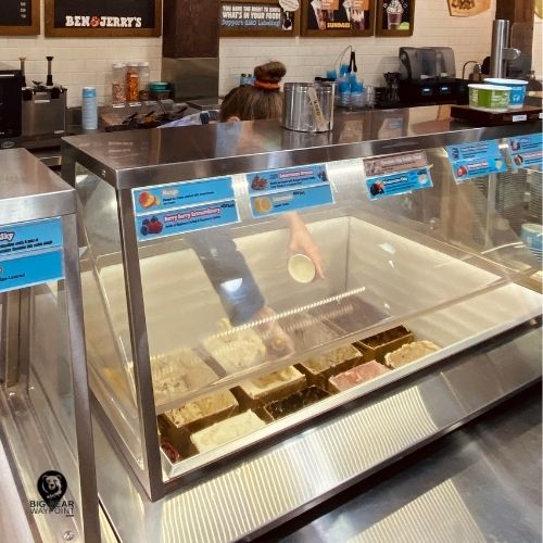 Ben and Jerry’s Big Bear staff scooping ice cream from the display case filled with assorted flavors.