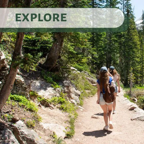 Two women hiking on a forest trail surrounded by pine trees in Big Bear Lake, California.