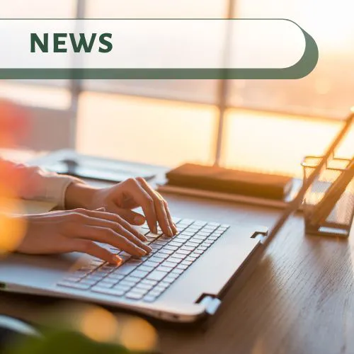 Hands typing on a laptop near a bright window at sunrise, representing Big Bear Lake news and updates.