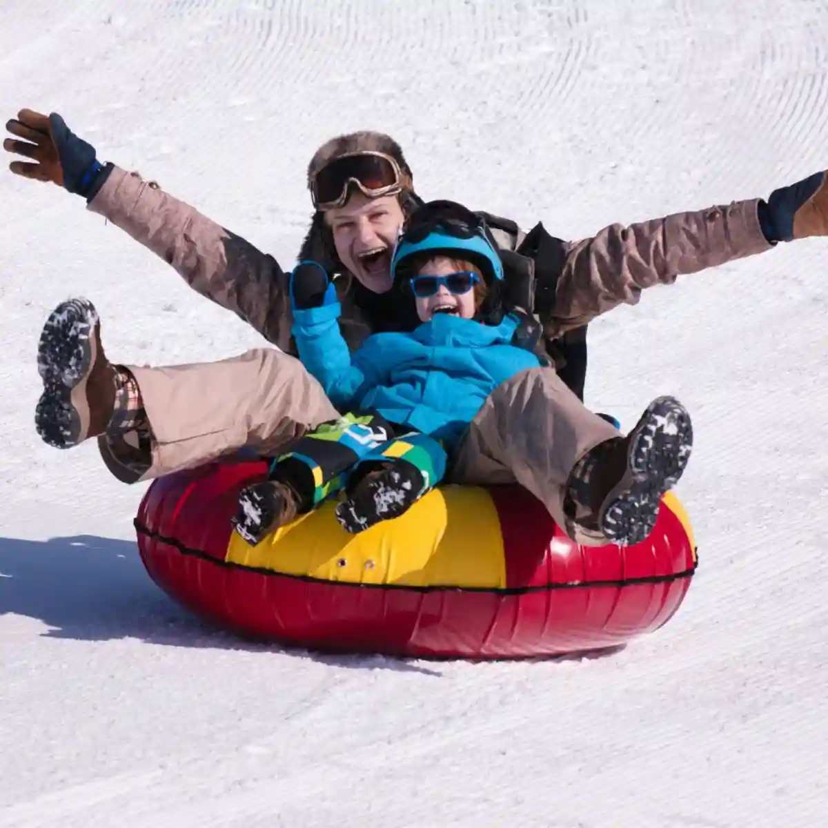 Two people smiling while snow tubing down a snowy slope at Big Bear Lake.