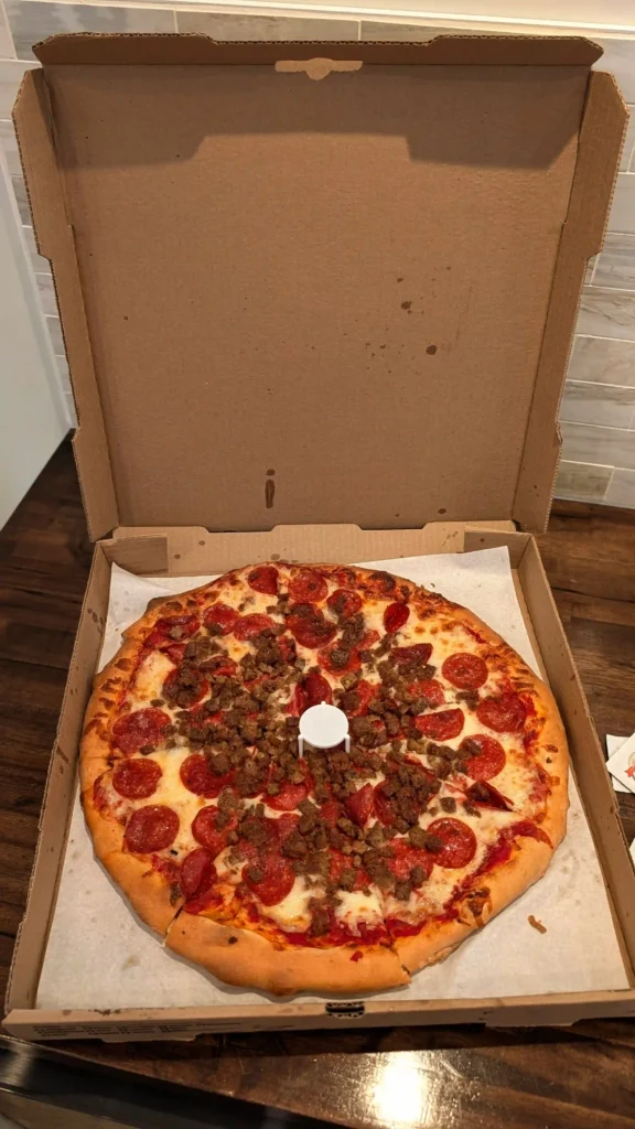 Large pepperoni and homemade Italian sausage pizza with melted mozzarella cheese inside a takeout box from Maggio's Pizza.
